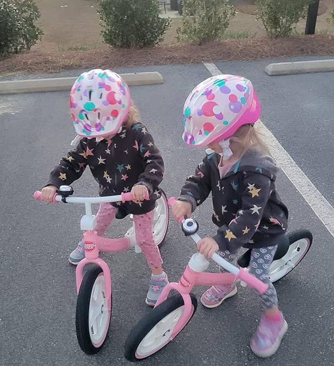 Two children with polka-dot helmets riding balance bikes