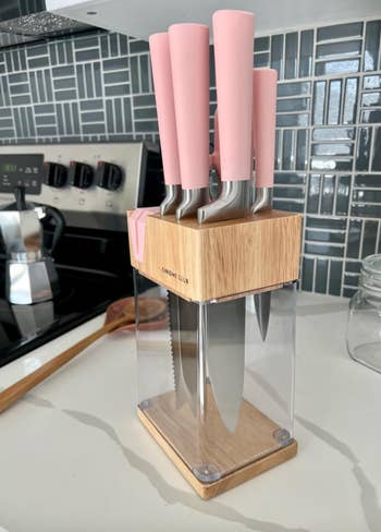 Knife set with pink handles in a wooden and acrylic block on a kitchen counter