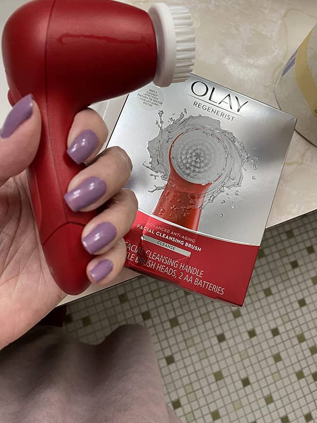 A reviewer holding the red facial brush with the box in the background