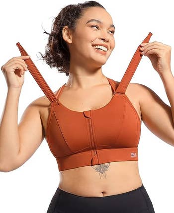 model adjusting the front closure straps on the orange sports bra