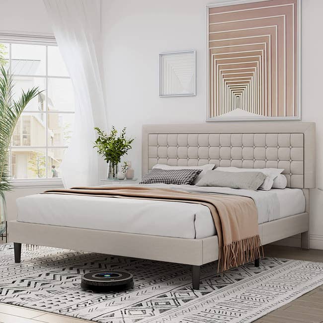 a beige upholstered bed frame with tuft detailing on the large headboard