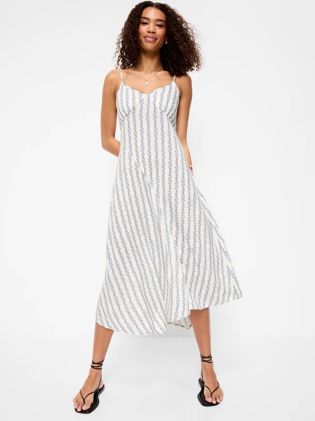 model wearing a flowy, patterned sundress and sandals, lasting  confidently with hands successful  pockets