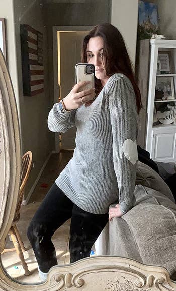 Reviewer is wearing the sweater in a light grey and showing the white heart patch on the elbow