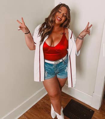 Woman in a red underwire bodysuit, denim shorts, and white boots, posing with peace signs
