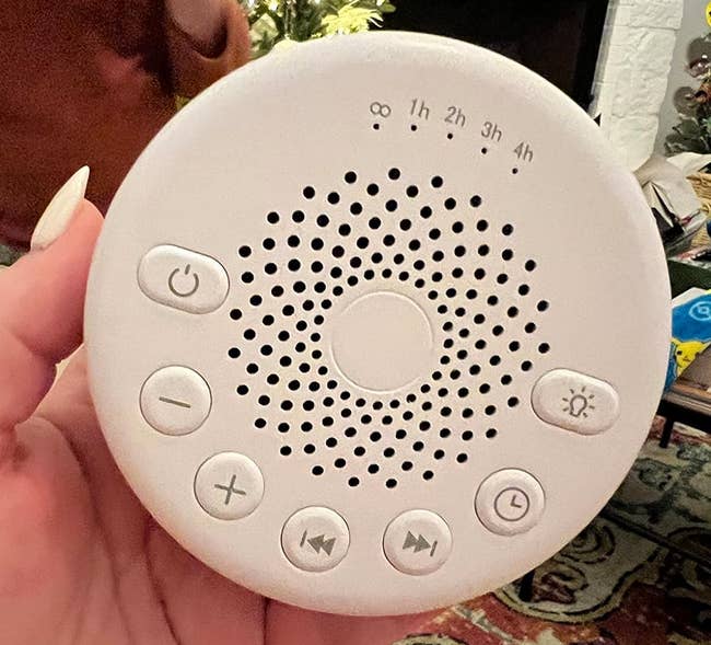 review holding a white, circular sleep sound machine with timer settings, volume, and power buttons