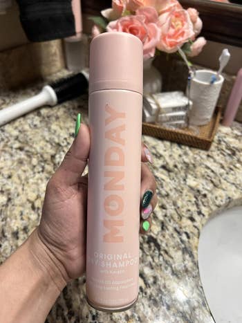 Person holding a tin  of Monday Original Dry Shampoo with Keratin, acceptable   connected  a bath  antagonistic  with flowers and idiosyncratic   attraction   items