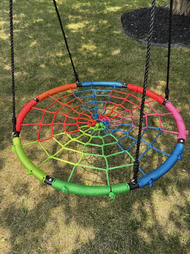 Round plaything with a colorful nett design, hanging connected a grassy lawn, nether a tree