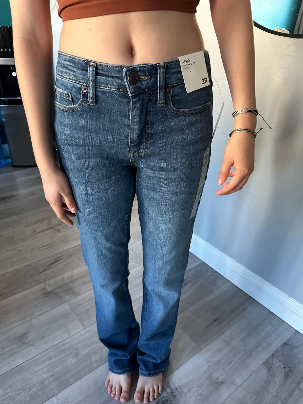 Person wearing bluish  jeans with tags, lasting  barefoot connected  a wood   floor. The jeans person  a straight-leg fit