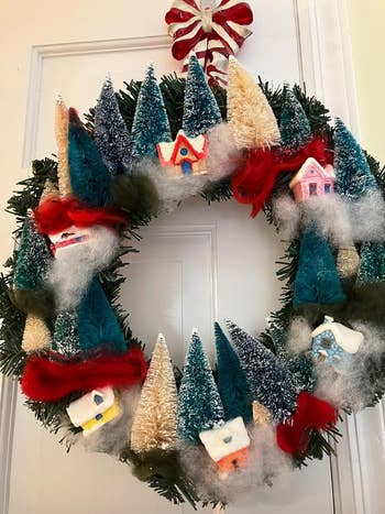 a close up a wreath with bottle brushes and tiny village houses hung on a reviewer's door