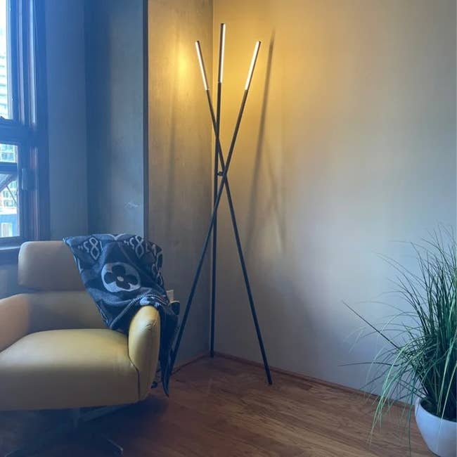 Reviewer image of tripod black metal floor lamp with lights on the end of each leg in the corner of a room next to a yellow chair