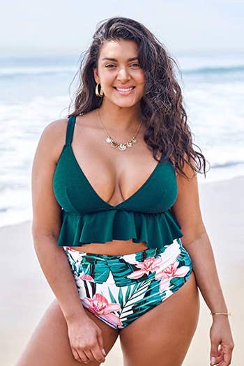 model wearing a forest green bikini top with a ruffle trip and high-waisted white bikini bottoms with a green and pink tropical print on them