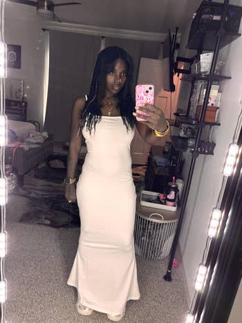 Person wearing a sleek, sleeveless dress poses for a mirror selfie in a room, showcasing a potential fashion purchase