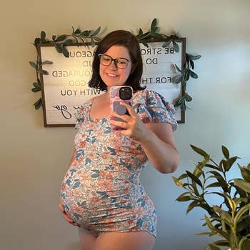 Person takes a reflector selfie successful floral maternity wear, smiling, with a leafy decorated motion successful the background