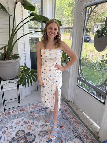 Person successful a strapless floral formal with a slit and level sandals, lasting successful a sunroom with a potted plant