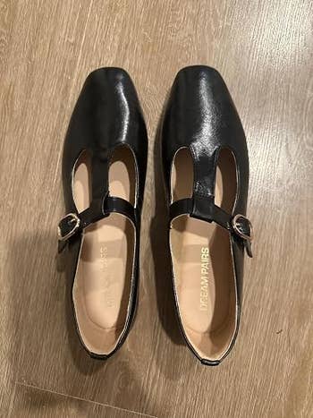 Black ballet flats with a quadrate  toed  plan  and buckle strap item  connected  a wood   floor