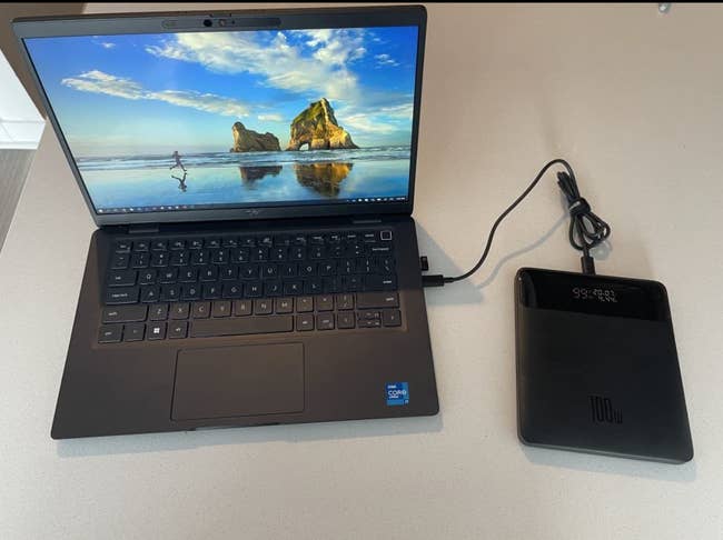 A reviewer's laptop connected to a small square shaped black charger bank