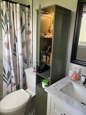Bathroom with a greenish  retention  cabinet, toiletries, and a decorative ablution  curtain featuring leafage  patterns