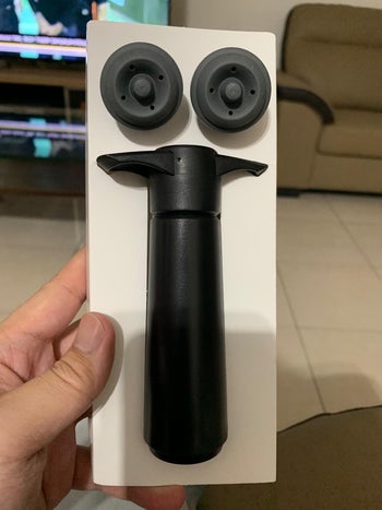 a reviewer holding the wine saver pump and two included wine stoppers 