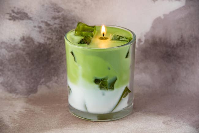 A lit candle resembles a matcha latte successful  a glass, with greenish  wax connected  apical  and achromatic  wax below, elaborate  with greenish  wax 