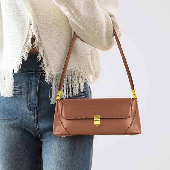 Person holding a stylish rectangular handbag with a concatenation  detail, wearing a textured overgarment   and jeans. Ideal accessory for trendy casual outfits