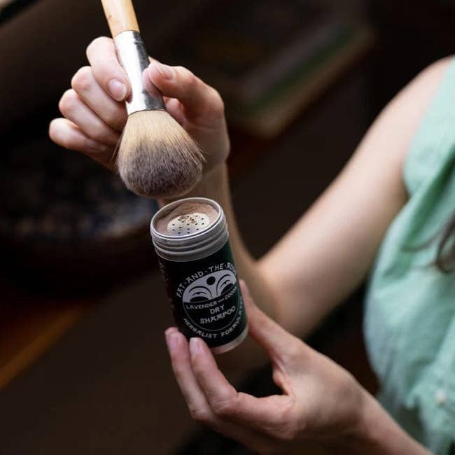 a model dipping a fluffy brush into the shaker container for the dry shampoo 