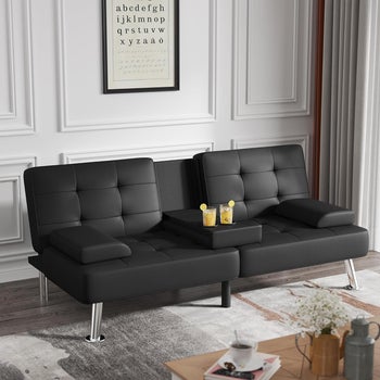 the black faux leather futon sofa in upright position with cupholders holding drinks