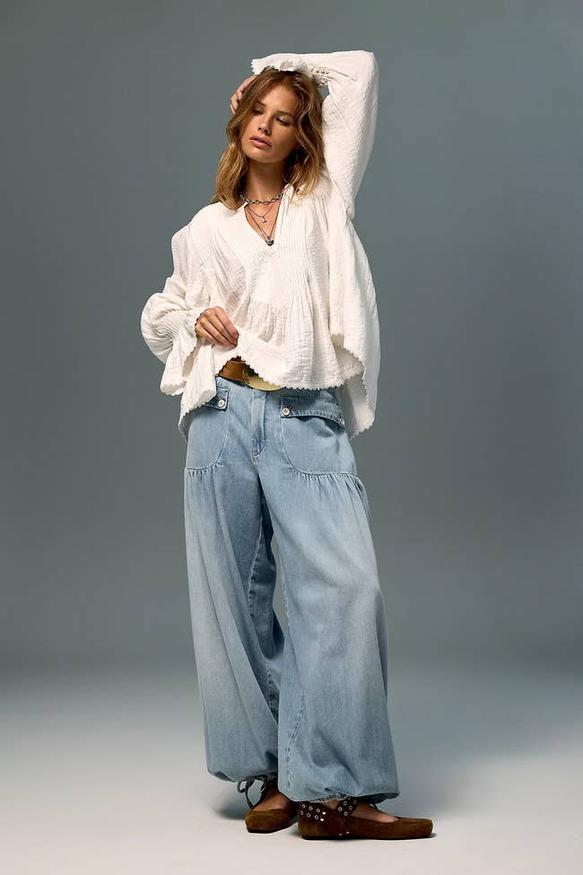 Fashion exemplary  wearing a escaped   achromatic  blouse and wide-leg denim jeans, accessorized with layered necklaces and brownish  ankle boots
