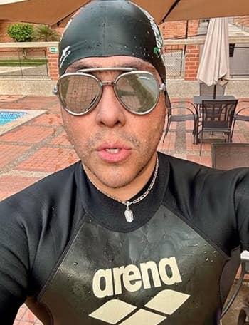 Person successful bedewed aquatics headdress and goggles wearing a branded wetsuit, lasting by a poolside lounge area