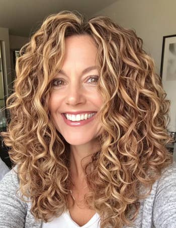 Person smiling with curly hair, wearing a casual grey  apical  indoors. Style suggests a relaxed, mundane  look