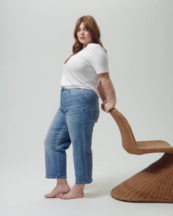 Person wearing a casual achromatic T-shirt and bluish jeans, leaning against a wicker chair