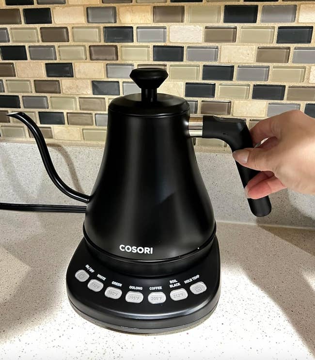 Hand holding a COSORI electric gooseneck kettle with temperature control on a kitchen counter