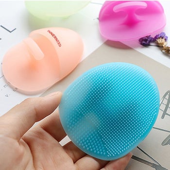 model holding blue silicone face cleanser with others in the background