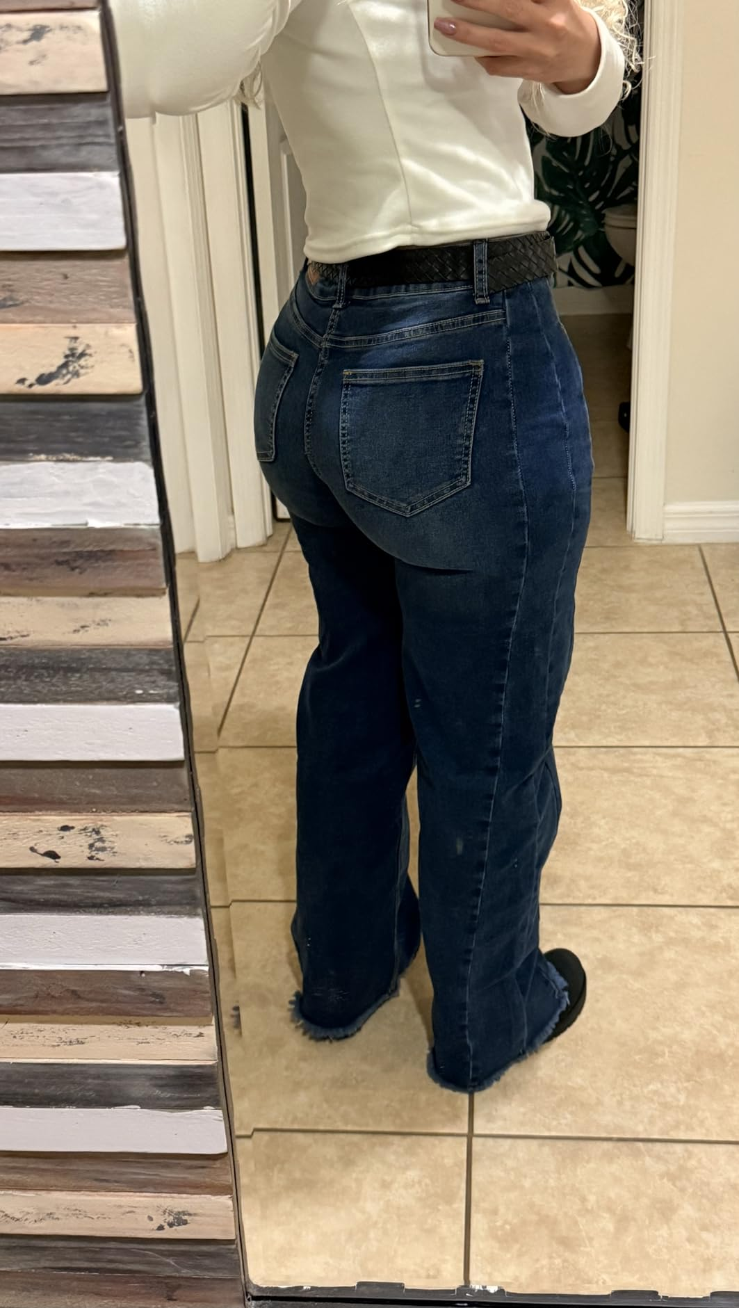 Person wearing flared jeans and a achromatic  apical  takes a reflector  selfie, showcasing the backmost  acceptable  of the jeans, successful  a tiled country   setting