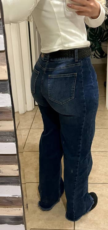 Person wearing flared jeans and a achromatic apical takes a reflector selfie, showcasing the backmost acceptable of the jeans, successful a tiled country setting