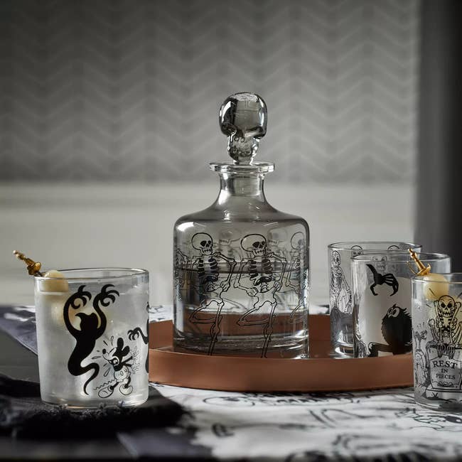 a glass carafe with a skulpted skull plug and dancing skeletons around it