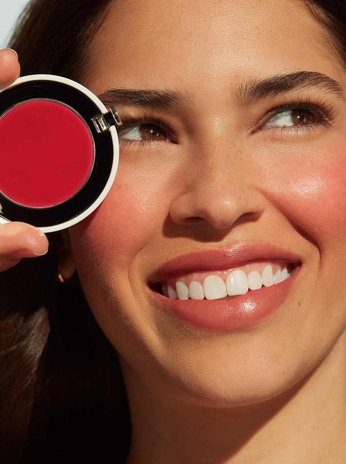 model wearing a light pink blush on cheek and lips and holding up the container of blush