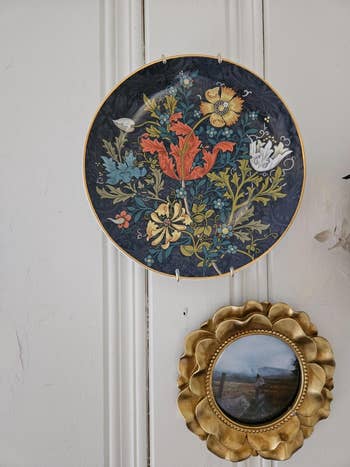 Decorative plates connected  wall; 1  shows a elaborate  floral pattern, the different   features a scenery  country   with a golden  scalloped frame
