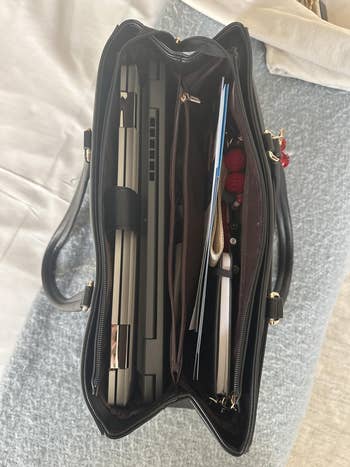 Open handbag with organized compartments, containing a laptop, documents, and pens. Ideal for business or school use