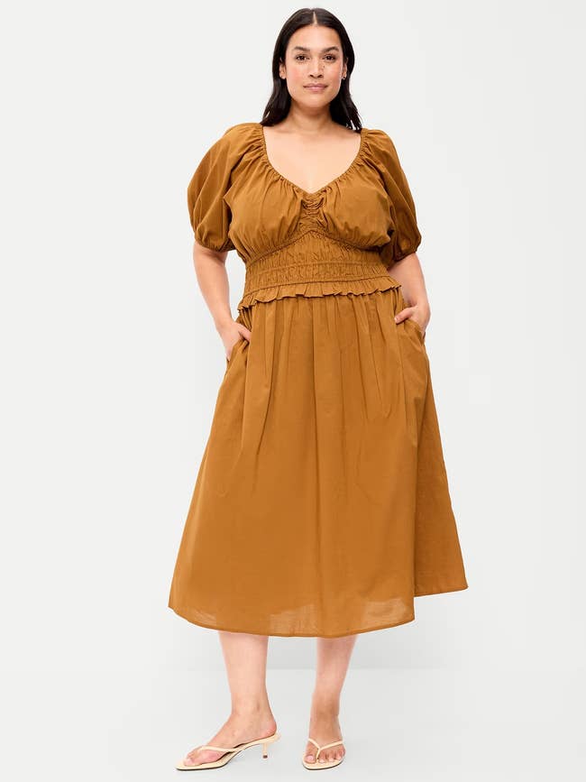 Model wearing a stylish, knee-length formal  with puffed sleeves and a ruched waist, paired with sandals, posing confidently