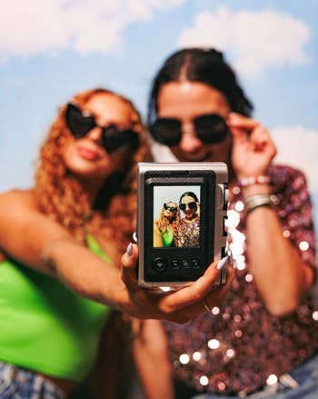 Two models taking a selfie with a black instant camera