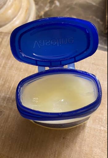 Open jar of petroleum jelly connected  a woody  surface, with the lid attached and resting open. Ideal for tegument  extortion  and moisture retention