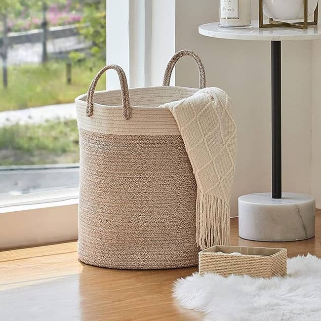 Photo of the half white and half wicker basket on floor, filled with blankets