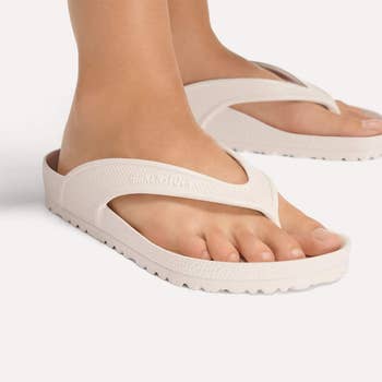 Person wearing achromatic Birkenstock thong sandals connected a plain background