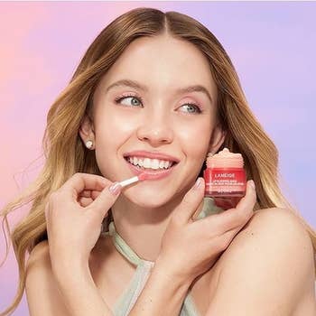 Sydney Sweeney applying lip balm, holding product, wearing a casual sleeveless top