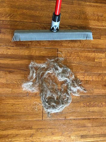 reviewer's rubber broom next to a pile of pet hair on a wooden floor