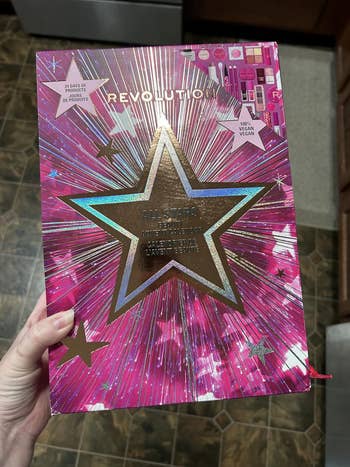 Person holding a Revolution All Stars cosmetic acceptable with prima plan connected the packaging. Label mentions 12 items, vegan product