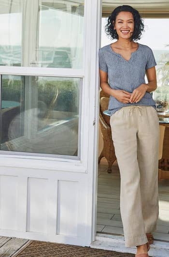 model wearing beige linen pants, leaning against doorway