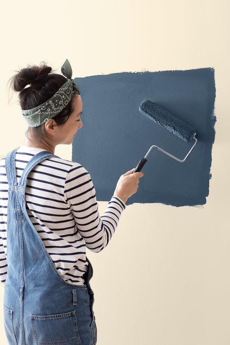A woman uses a paint roller on a wall.