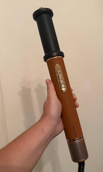 Person holding a handheld hairsbreadth styling instrumentality with a cylindrical plan and buttons connected the handle