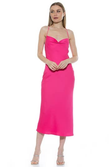Person wearing a sleek, sleeveless pink midi dress with spaghetti straps, posing on a plain background